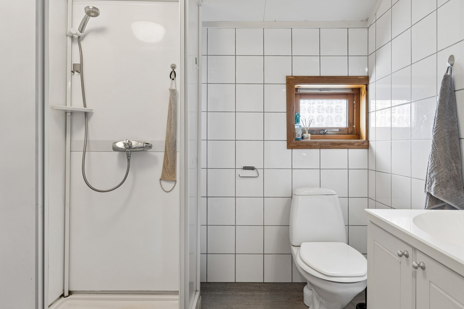 Badet i andre etasje har vinylbelegg på gulv, fliser på veggene og et praktisk dusjkabinett. Galleribilde