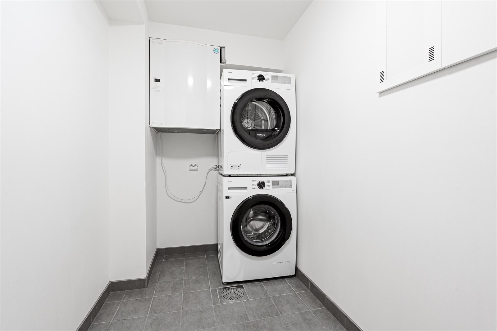 Praktisk, separat vaskerom med flislagt gulv, opplegg for vaskemaskin og boligens balanserte ventilasjonsanlegg. Galleribilde