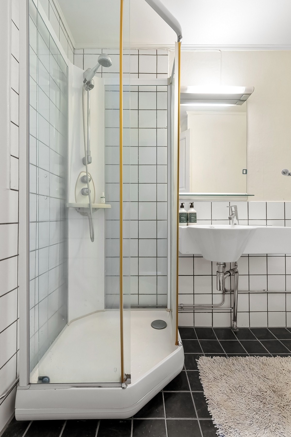 Tidløst og romslig bad med varmekabler. Badet inneholder servant med speil og lys over, toalett og dusjkabinett med skyvedører. Galleribilde
