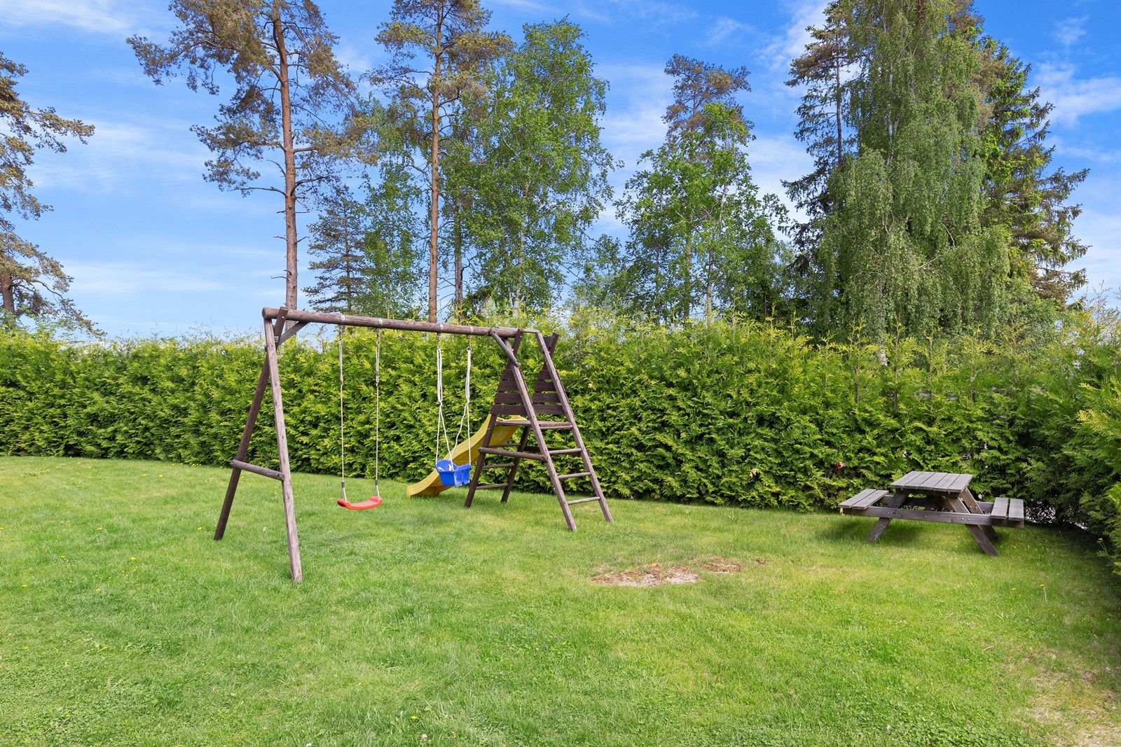 Fellesområdet inkluderer en lekeplass med husker og piknikbord, omgitt av grøntarealer. Galleribilde