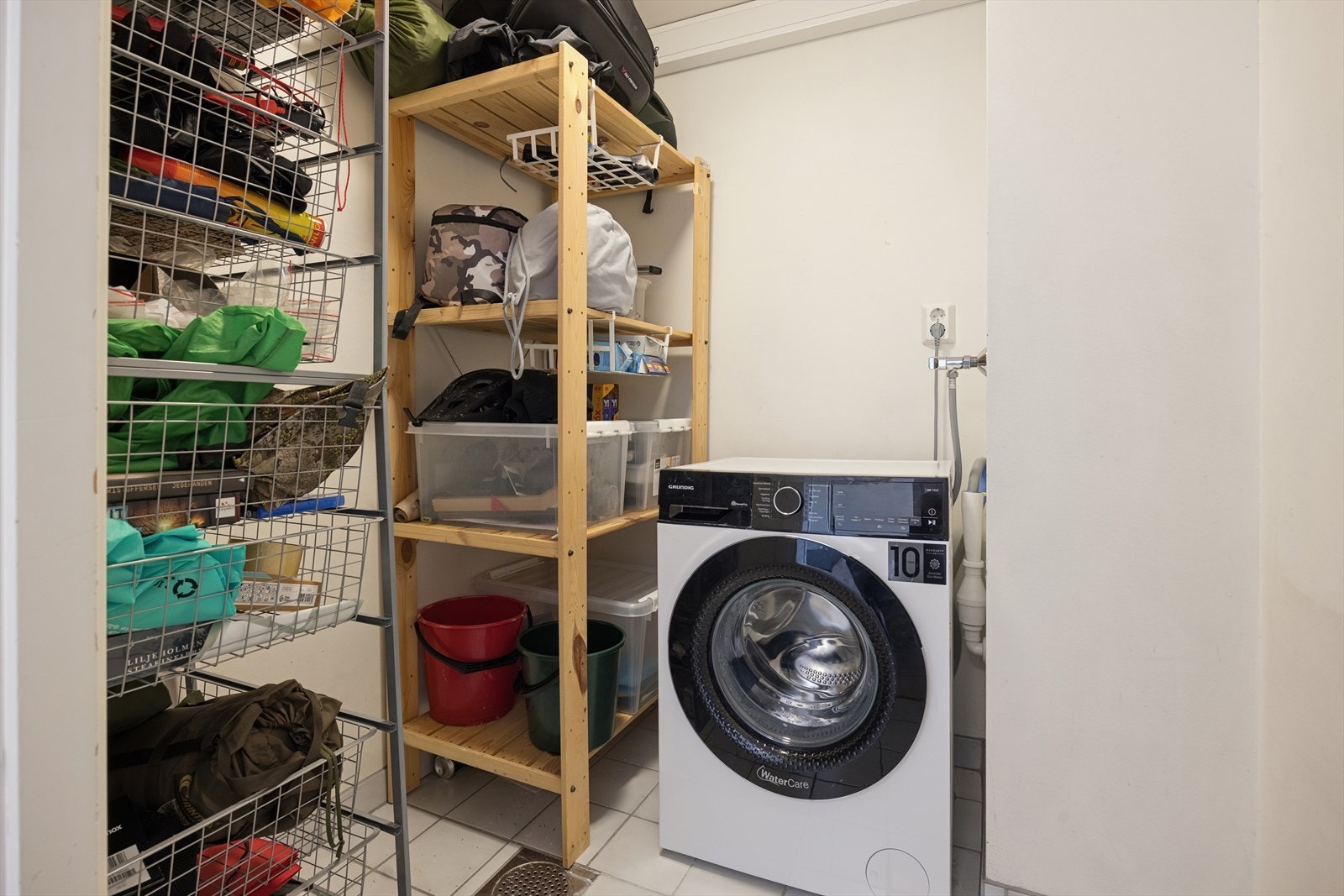 Innvendig bod med flislagt gulv, sluk og opplegg for vaskemaskin. Galleribilde