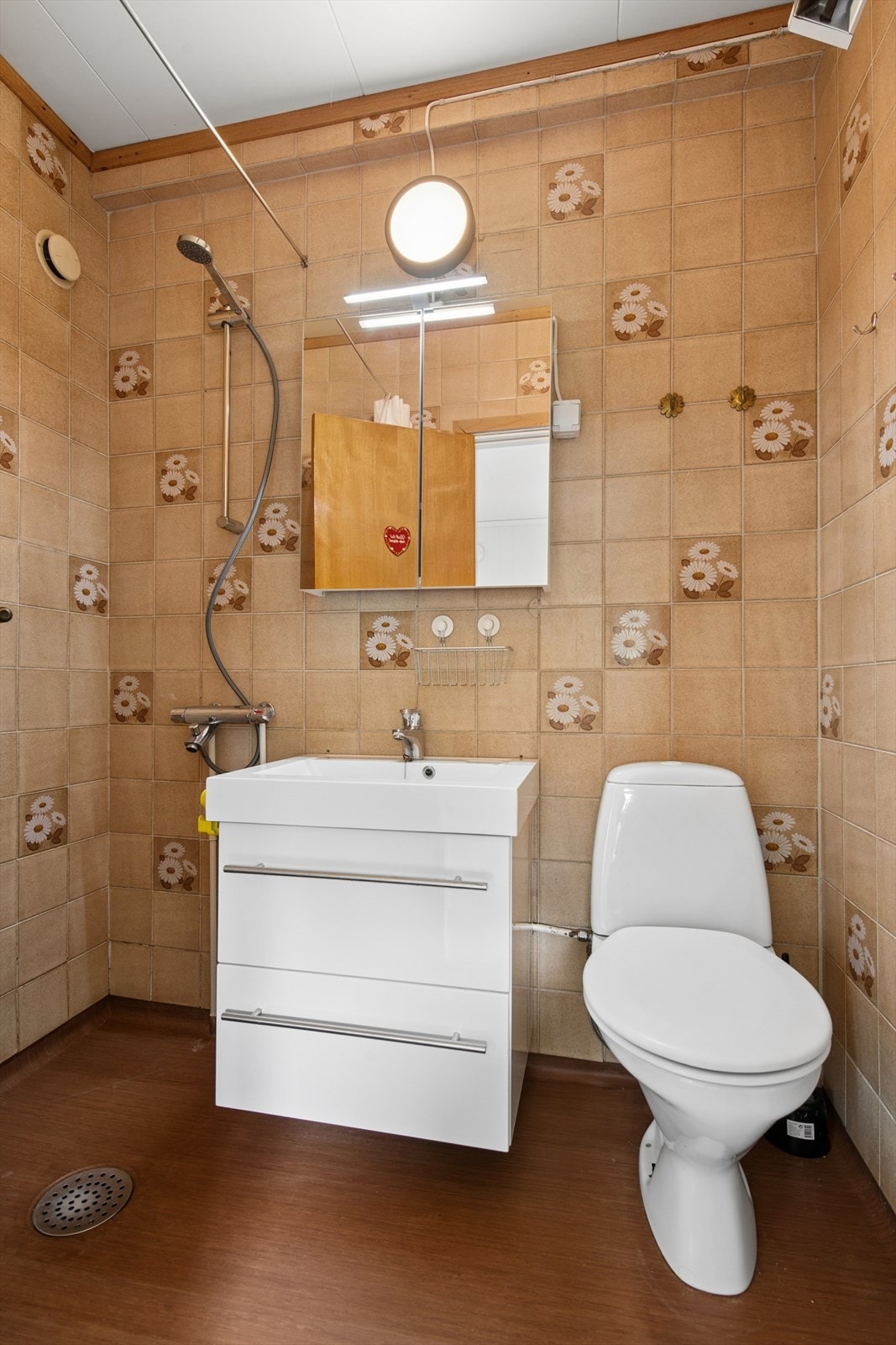 Badet er utstyrt med gulvmontert toalett, servant med underskap og dusj med forheng. Galleribilde