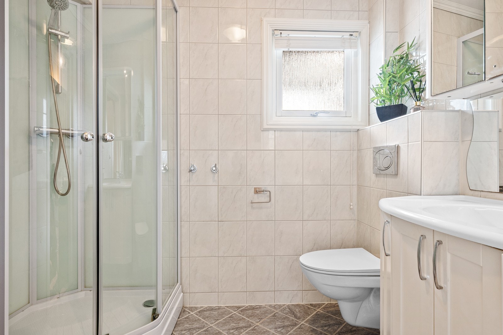 Badet i første etasje med flislagt gulv med elektriske varmekabler, veggmontert toalett og dusjkabinett. Galleribilde