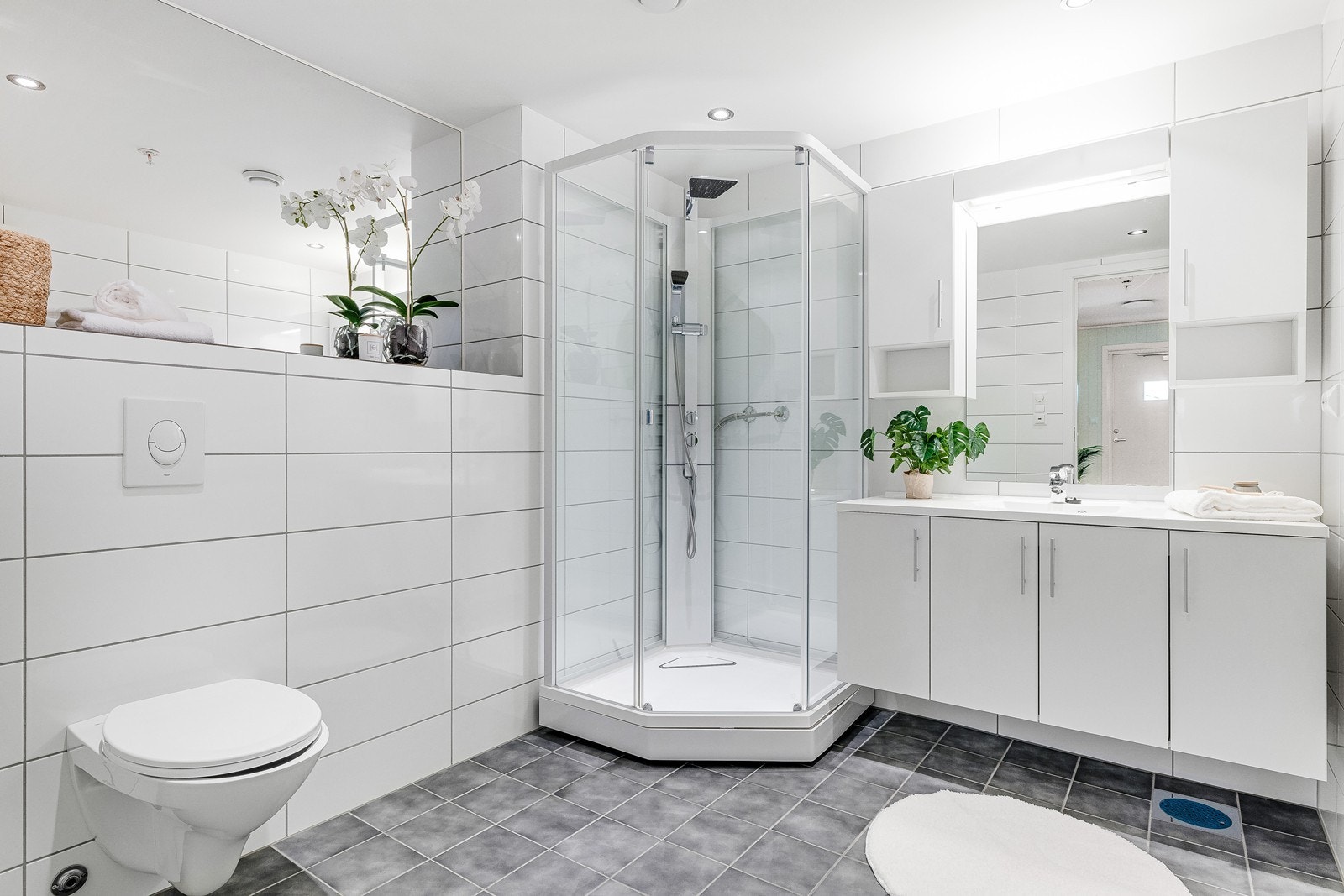 Badet fremstår som lyst og stilrent med flislagte flater i nøytrale fargetoner. Her er det vegghemgt toalett, dusjkabinett og servant med underskap og speil. Galleribilde