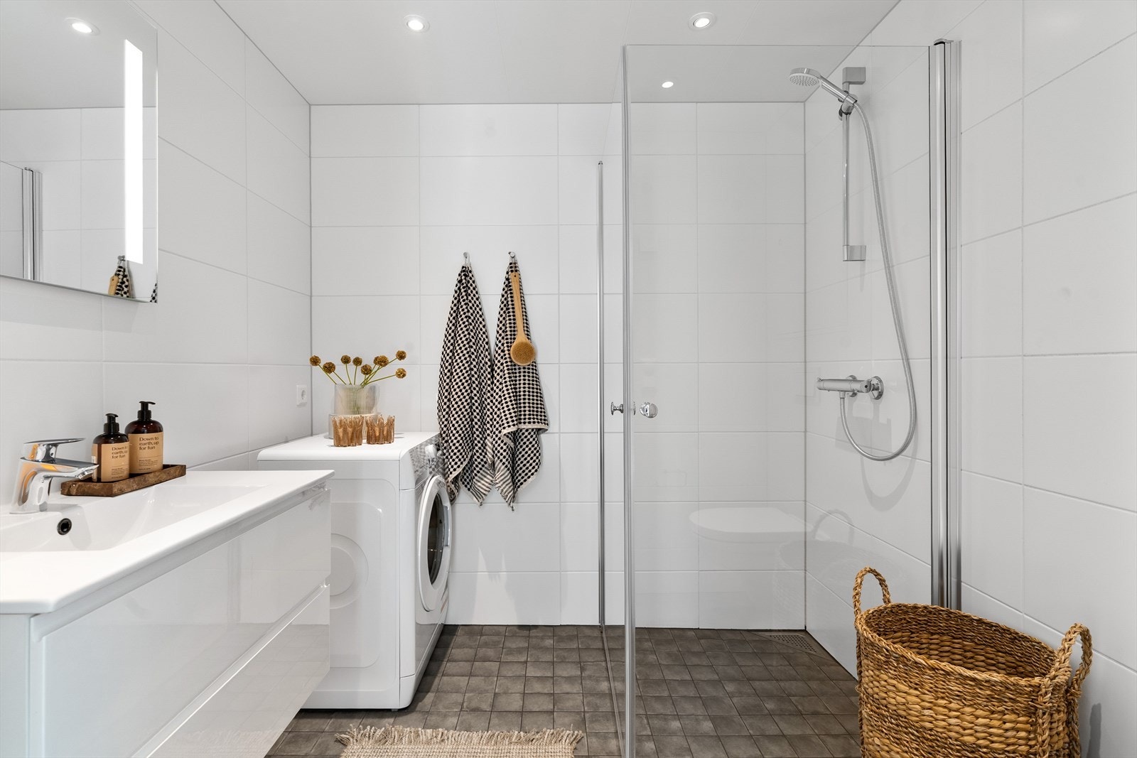 Badet byr på veggfestet innredet servant, praktiske innfellbare dusjdører, opplegg for vaskemaskin og vegghengt toalett. Galleribilde