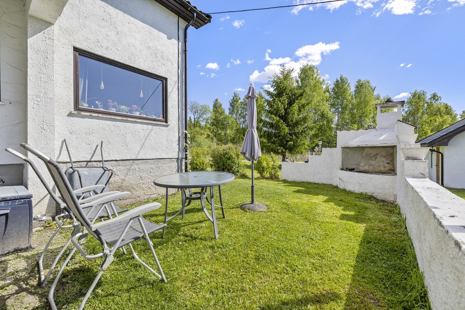 Boligen ligger i et svakt skrånende terreng med gressplen og gruset gårdsplass. Galleribilde