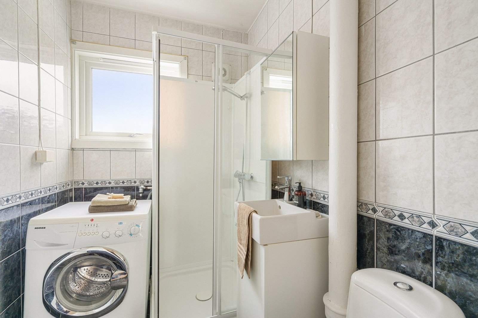 Badet er flislagt og innredet med toalett, vask i seksjon og dusjkabinett. Det er opplegg for vaskemaskin. Galleribilde