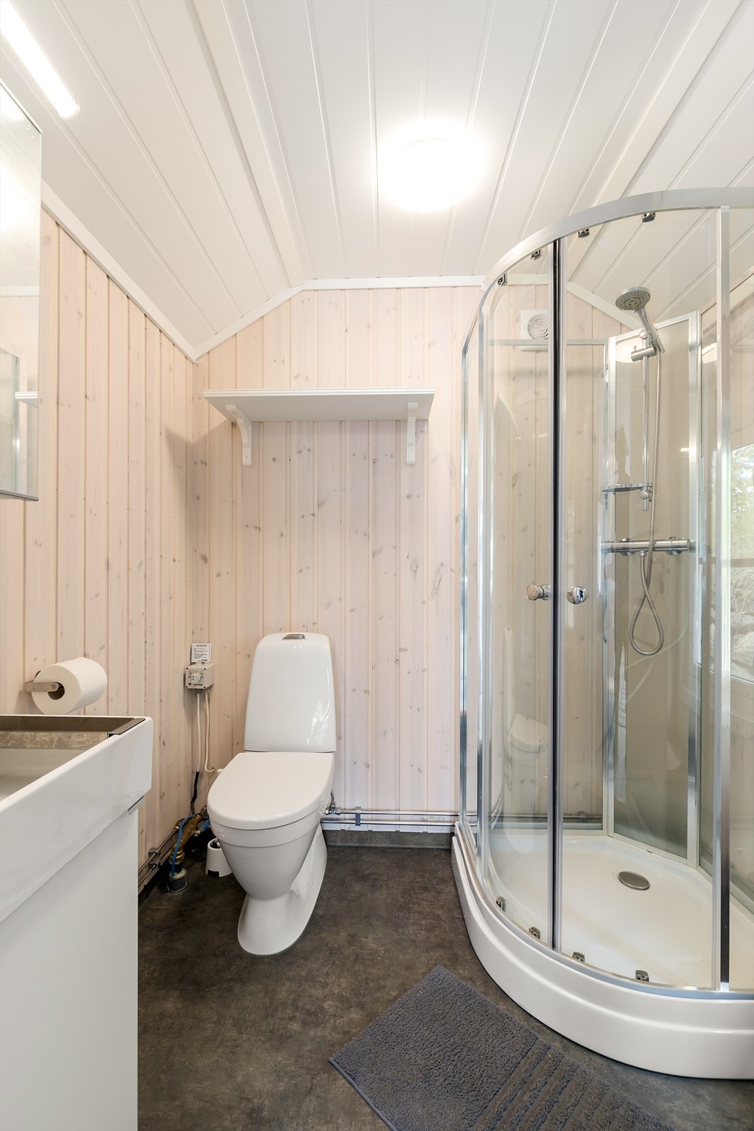 Badet har belegg på gulv og panel på vegger, og inneholder dusjkabinett, WC og servant med skap. Galleribilde