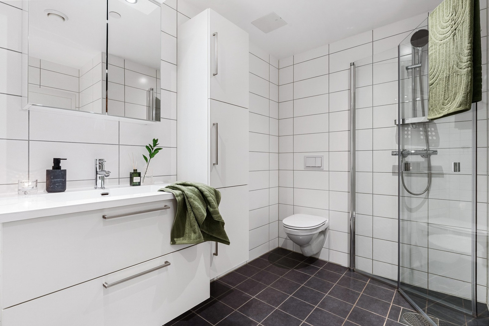 - Badet fremstår lyst og klassisk med flislagte overflater, vegghengt toalett, helstøpt servant med skuffeløsning, dusj med glassdører og opplegg for vaskemaskin - Galleribilde