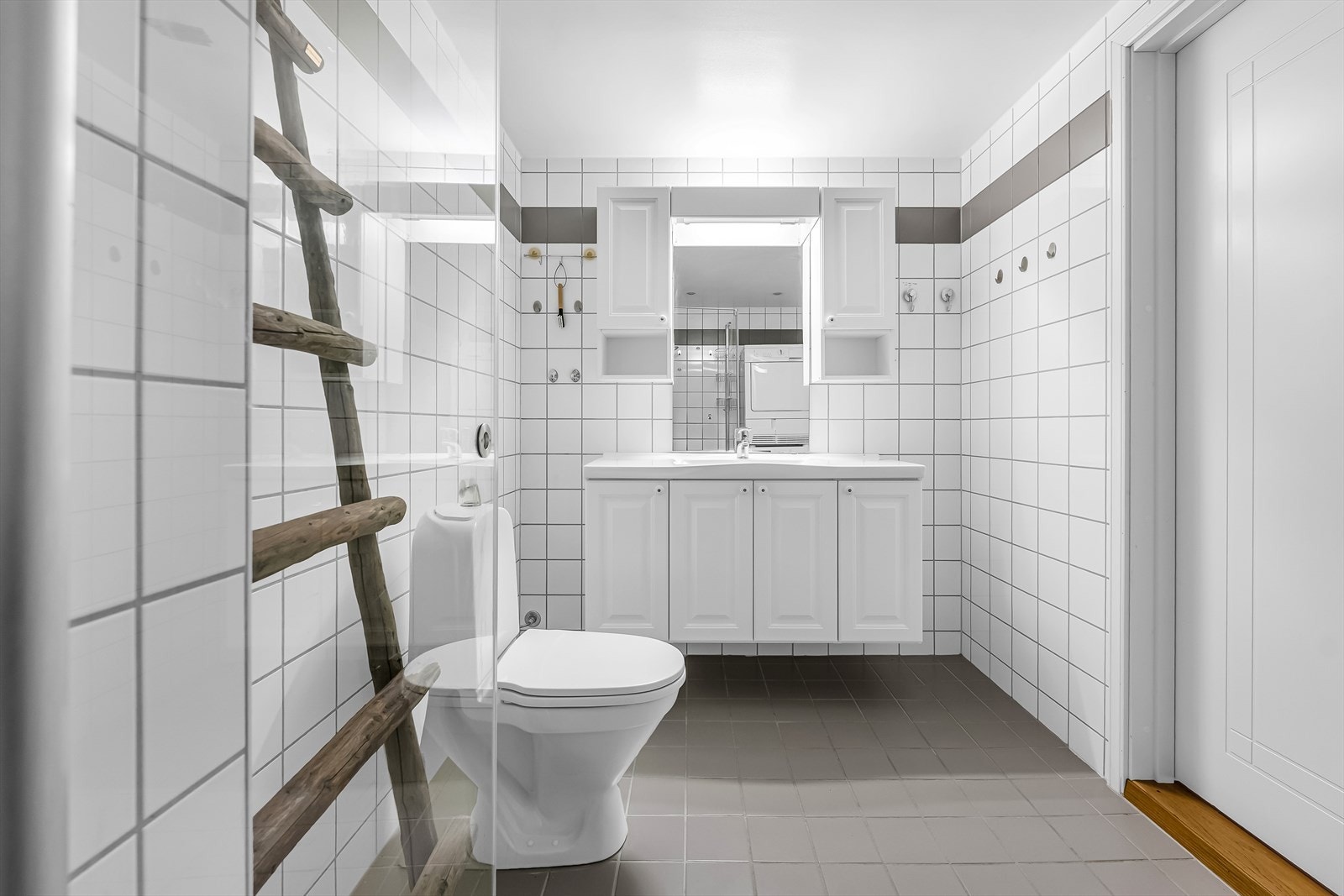 Badet er utstyrt med gulvmontert toalett. Det er nisje med opplegg for vaskemaskin. Dusjnisje med hånddusj og dusjdør i glass. Galleribilde