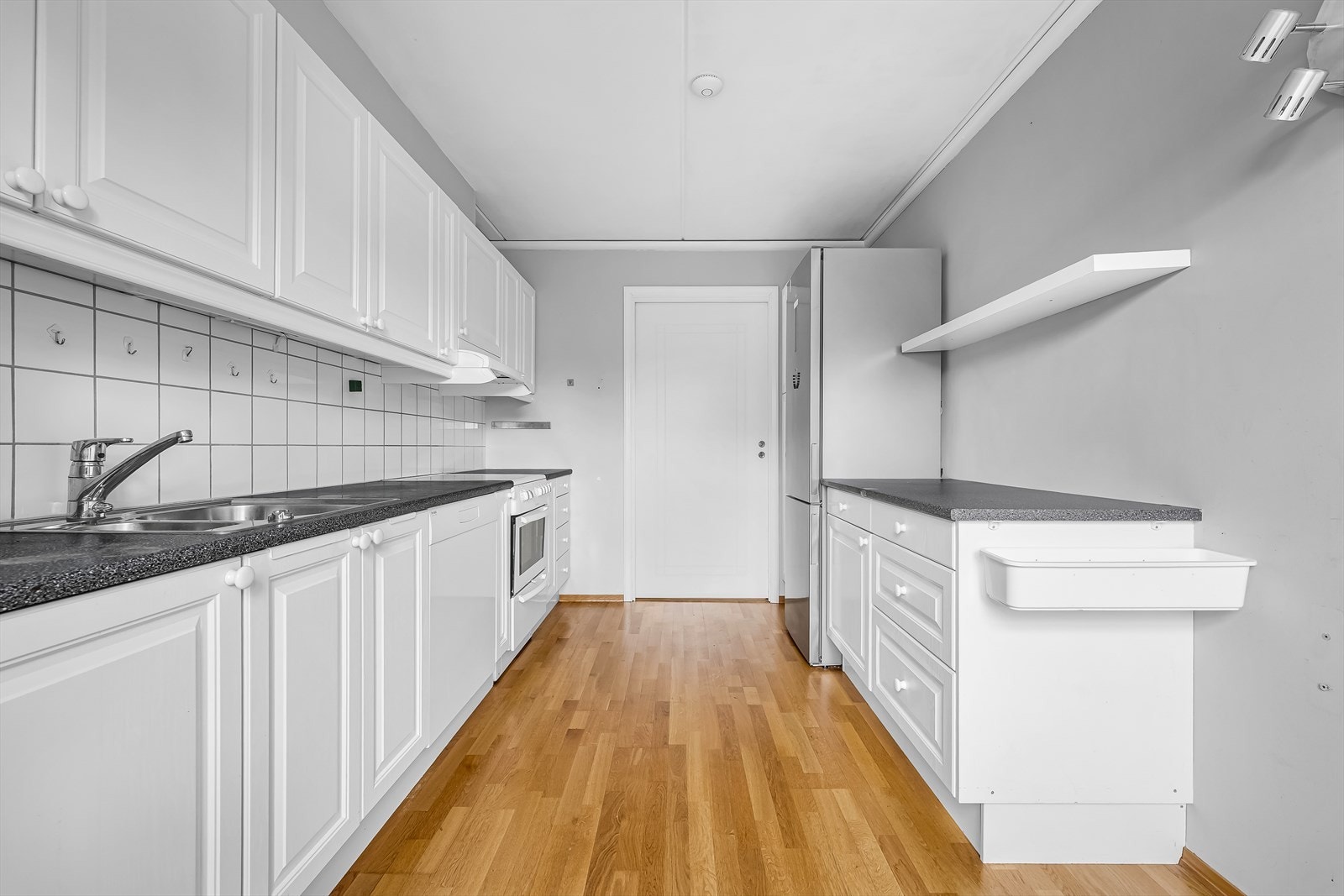 Kjøkkeninnredning fra byggeår med klassiske, profilerte hvite fronter. Laminert benkeplate med nedfelt stålkum og ettgreps blandebatteri. Tilrettelagt for kjøl/frys, komfyr og oppvaskmaskin. Integrert ventilator med avtrekk. Galleribilde