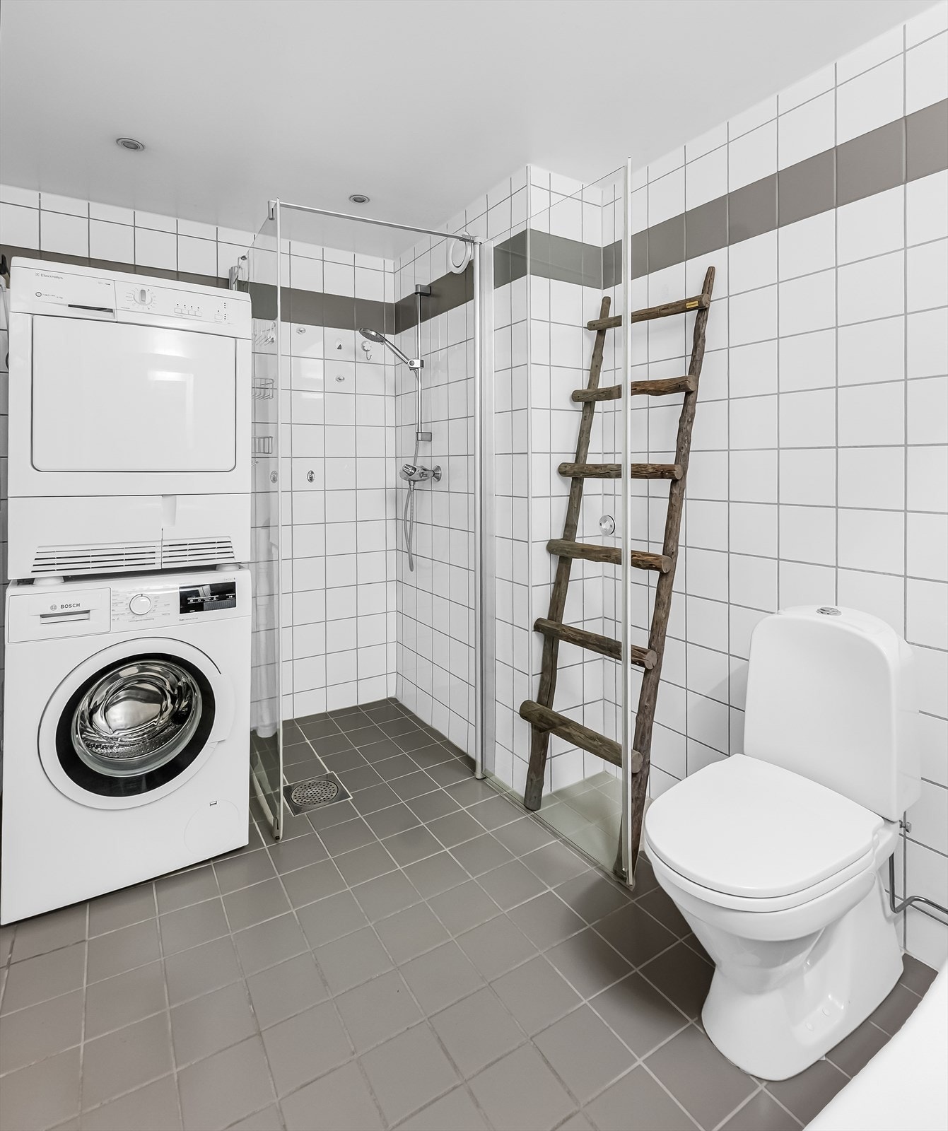 Badet er utstyrt med gulvmontert toalett. Det er nisje med opplegg for vaskemaskin. Dusjnisje med hånddusj og dusjdør i glass. Galleribilde