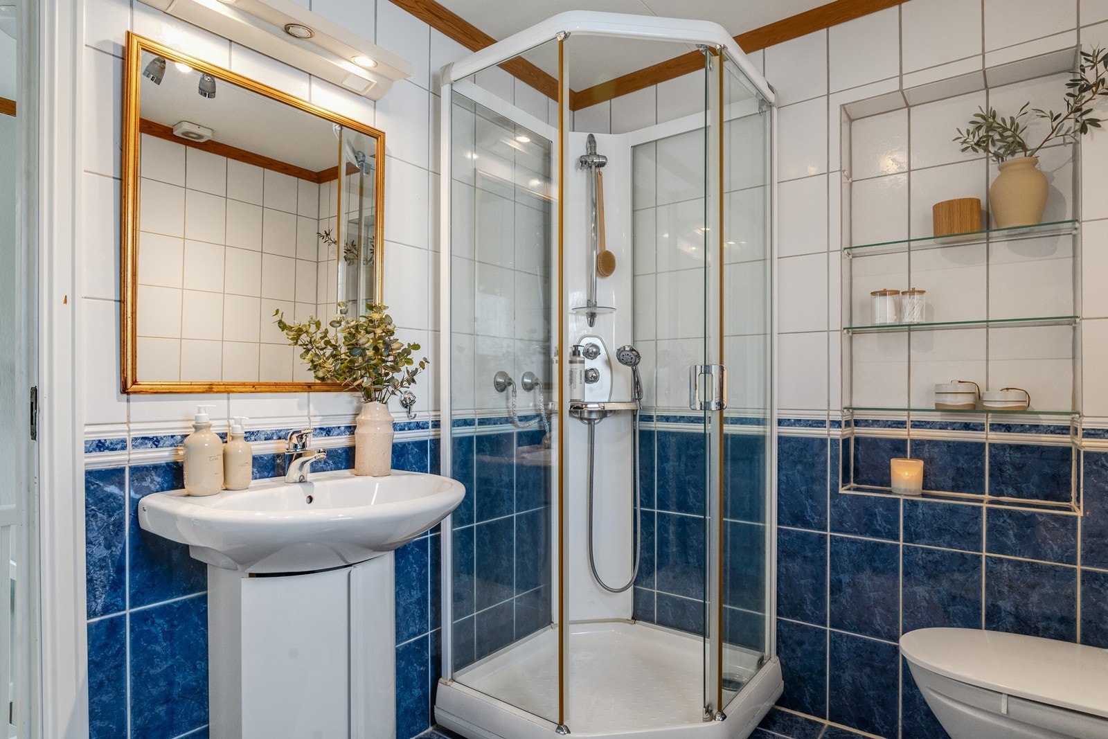Badet er helfliset og inneholder servant, speil, belysning, dusjkabinett og toalett. Galleribilde