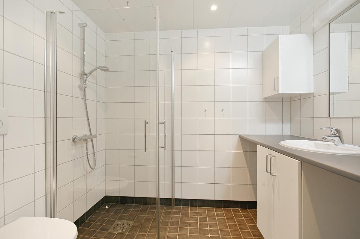 Romslig baderom med flislagte overflater, elektriske varmekabler og opplegg for vaskemaskin. Galleribilde