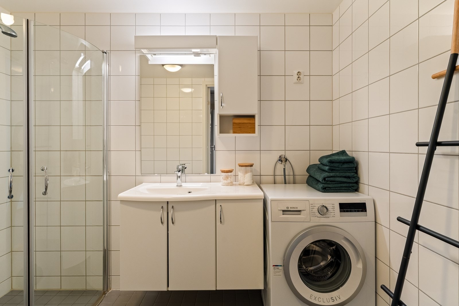 Badet er innredet med benkeskap med servant, dusjdører, gulvmontert toalett og opplegg for vaskemaskin Galleribilde