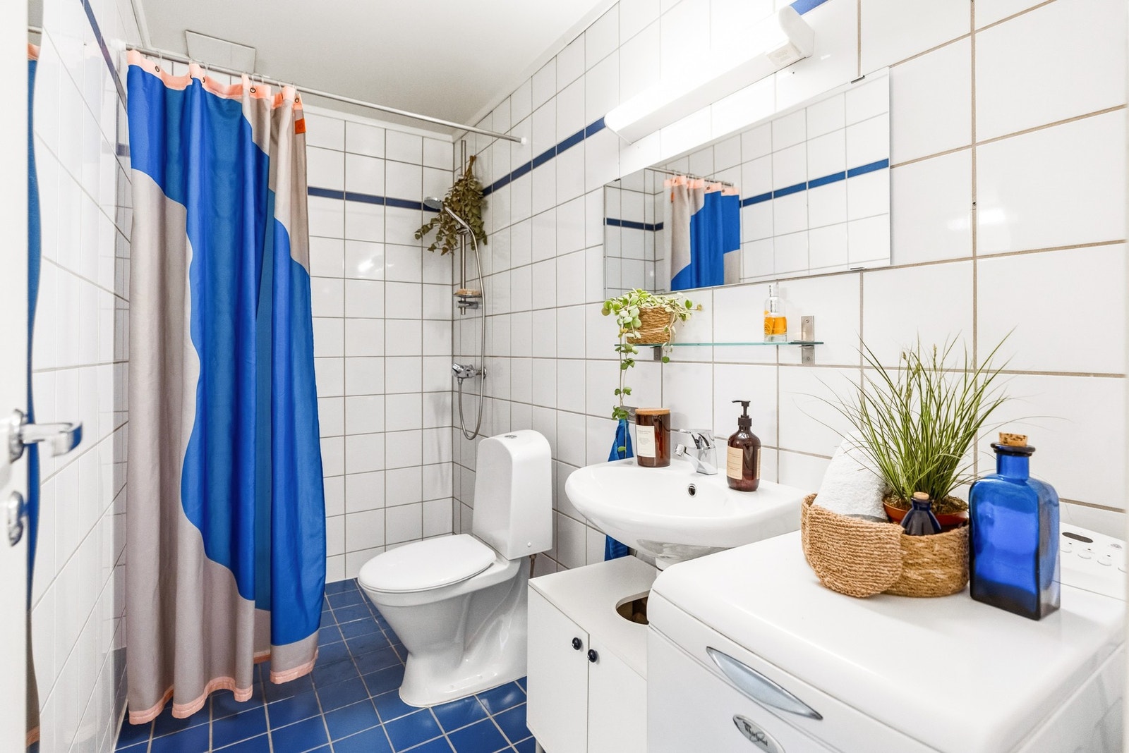 Baderom utstyrt med gulvstående klosett, servant med skap, dusj på gulv og opplegg for vaskemaskin. Galleribilde