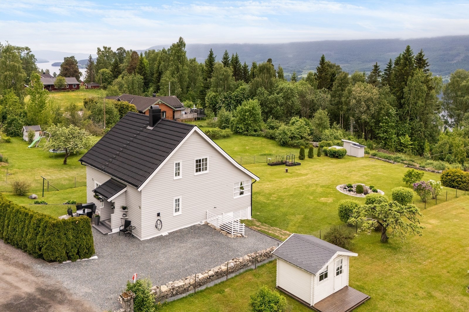 Gruset gårdsplass med hekk mot vei og dels steingjerde. Egen inngang til kjeller og vaskerom. Installert elbil lader på yttervegg. Galleribilde