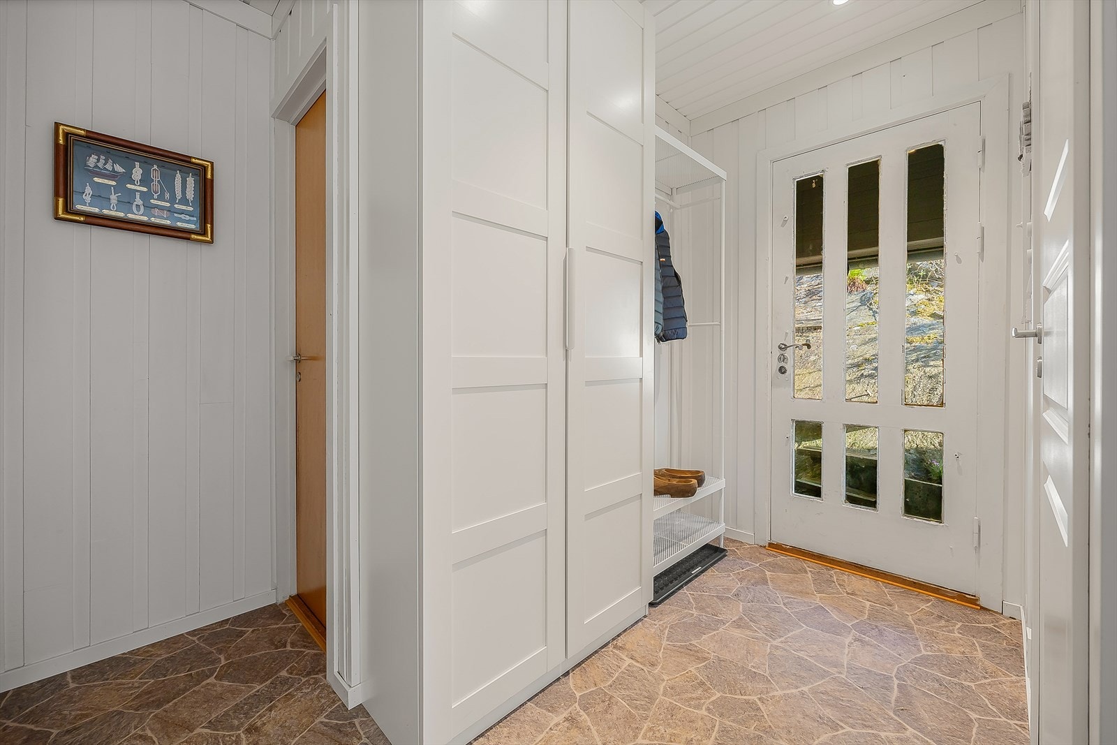 Entré med garderobeskap for oppbevaring av yttertøy. Gulvet har belegg og veggene har malt panel. Galleribilde
