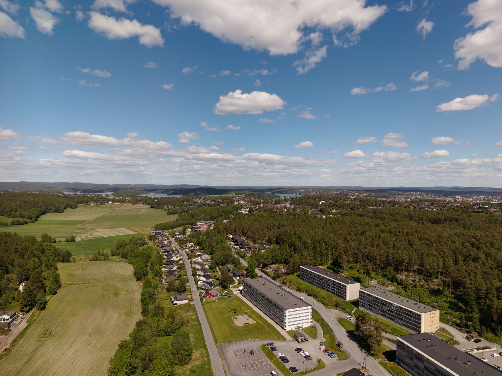 Dronebilde viser store fellesområder med rikelig av parkeringsplasser. Trygg skolevei nedenfor blokka og nærhet til Grålum og aktivitetssenter - samt nærhet til E6 for pendlere Galleribilde