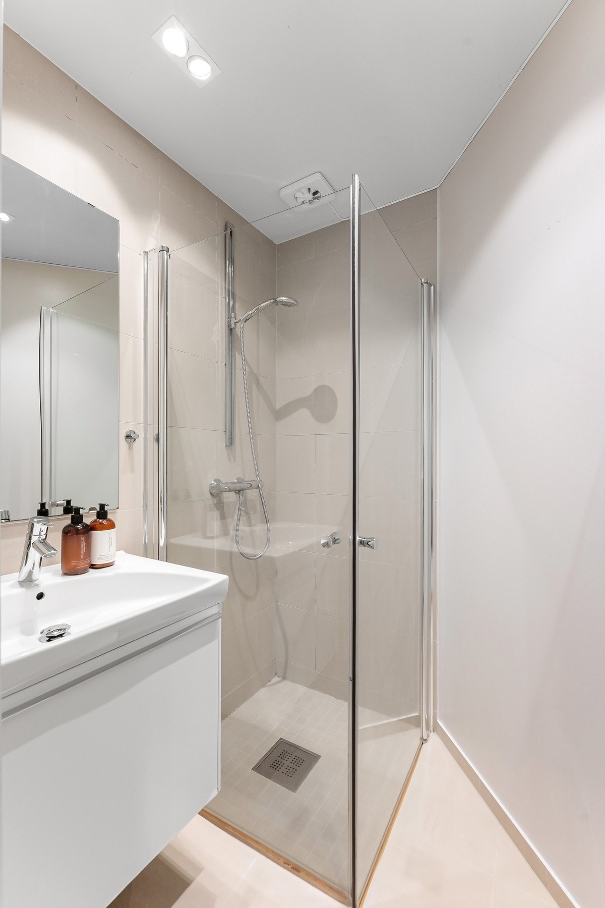 Badet fremstår moderne og innbydende med delikate flislagte overflater i lyse, tidløse toner Galleribilde