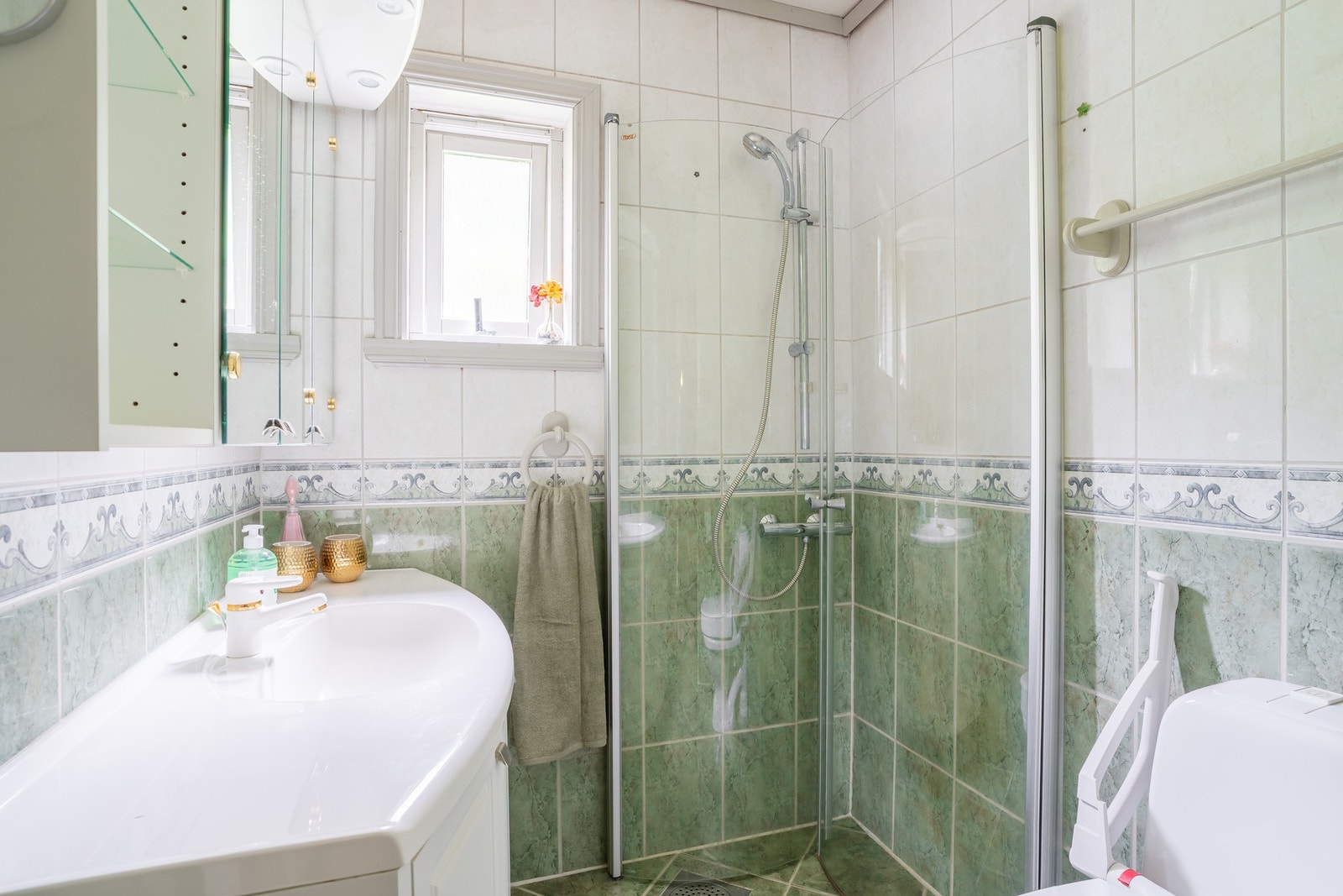 Badet er innredet med toalett, dusjhjørne med glassvegger, og baderomsmøblement med speil og belysning. Galleribilde
