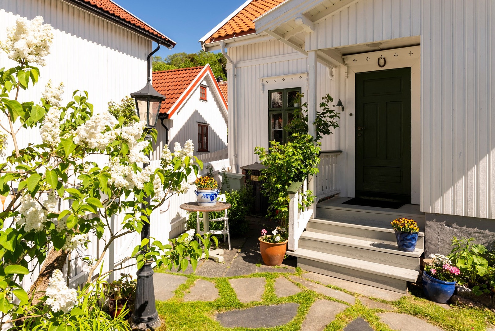 Et koselig og frodig uteområde med syriner, skiferheller og sjarmerende trehusbebyggelse rundt Galleribilde