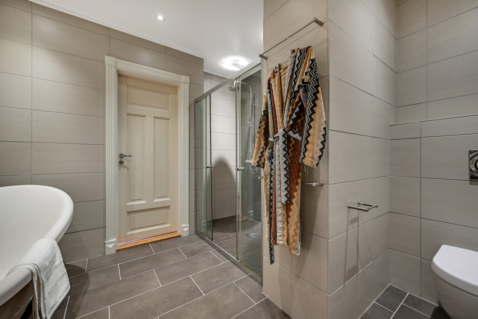 Badet er innredet med badekar, vegghengt klosett, dusjvegger og baderomsinnredning Galleribilde