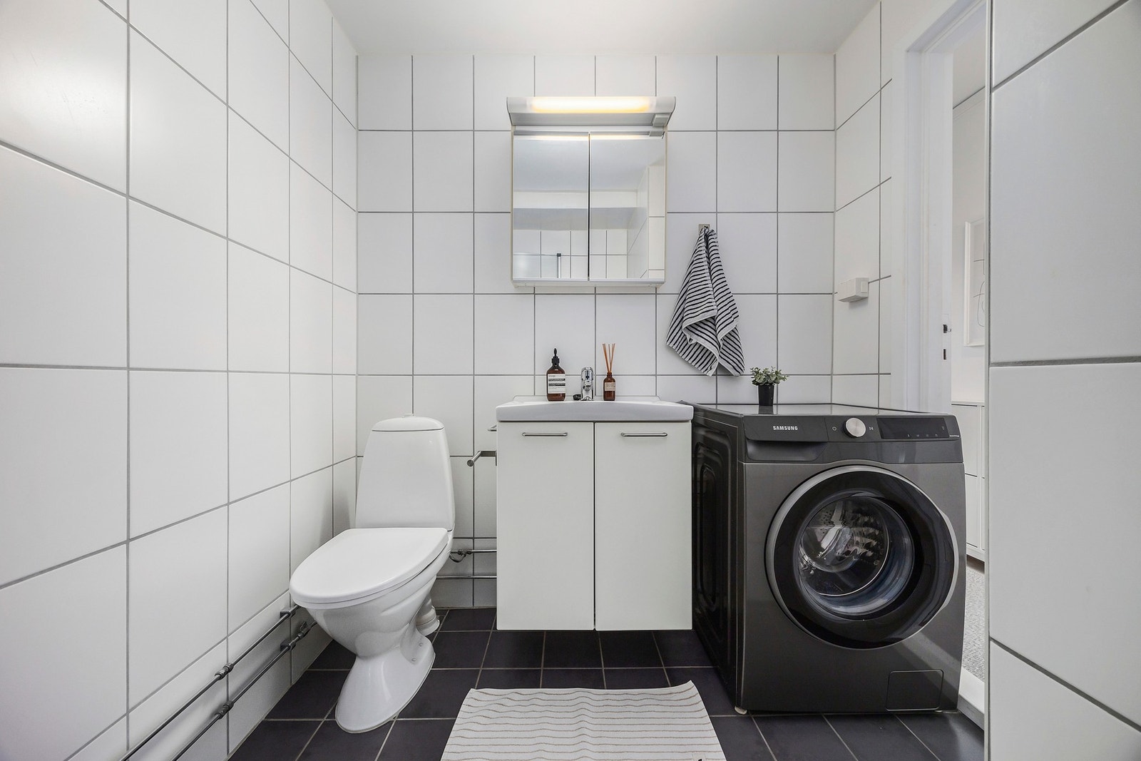 Flislagt bad med wc, baderomsinnredning, dusj og opplegg for vaskemaskin Galleribilde