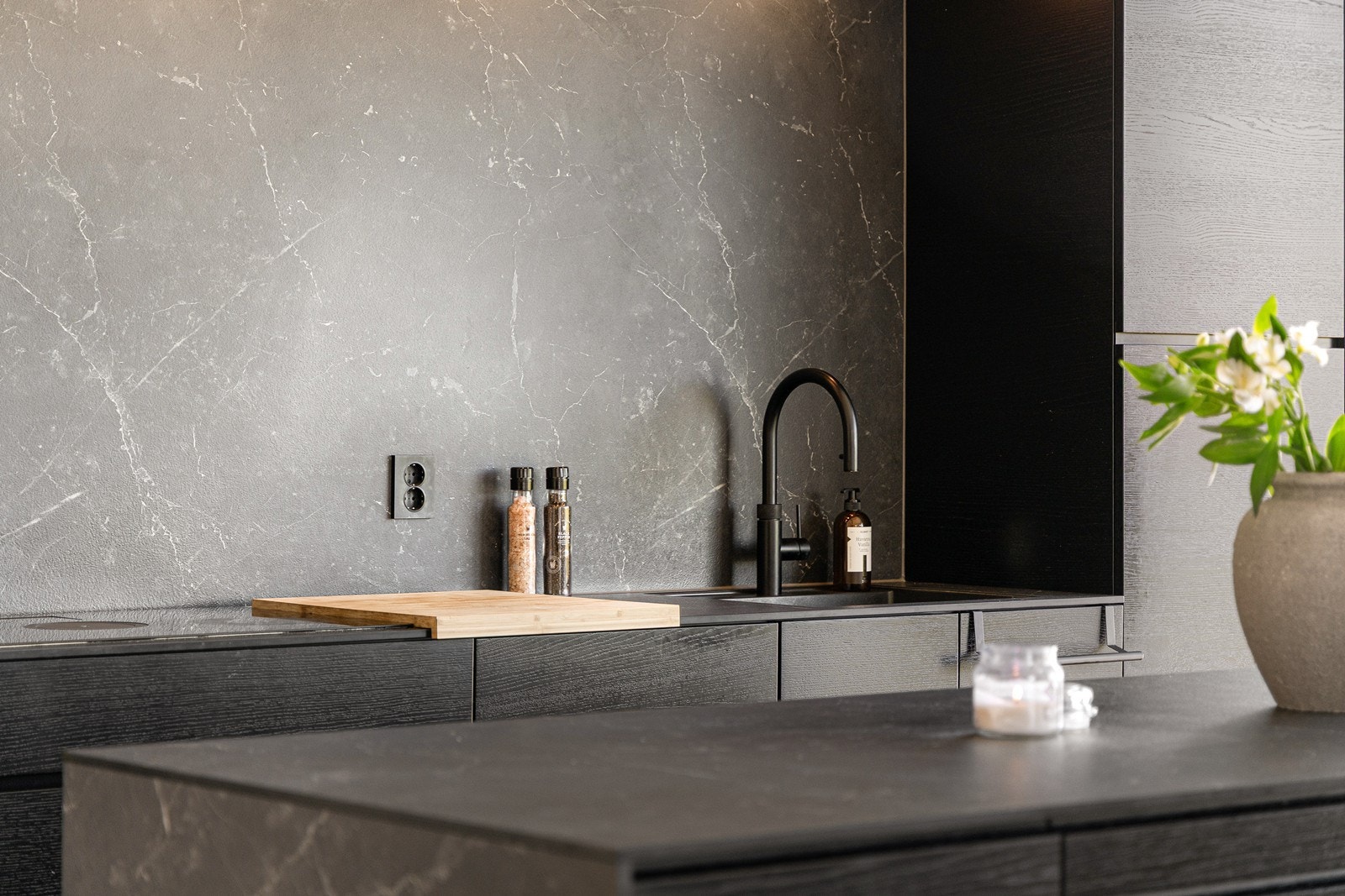 Benkeplaten er trukket ned langs sidene på kjøkkenøya og også brukt som backsplash over benken - noe som forsterker det helhetlige inntrykket. Galleribilde