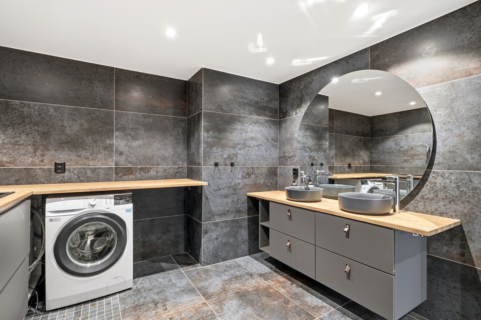 Badet har innredning med 2 servanter, vaskeroms-innnredning med benkeplate og nedfelt vask, veggmontert toalett, dusjvegger/hjørne og opplegg for vaskemaskin. Galleribilde