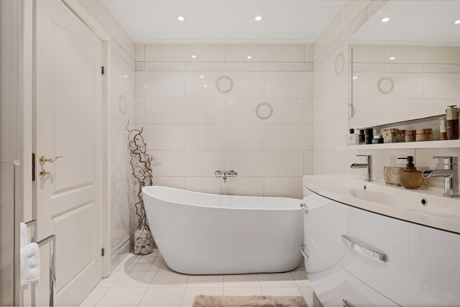 Videre er badet utstyrt med vegghengt toalett med innebygd sisterne, baderomsinnredning med dobbel servant, hylle og speil med integrert belysning Galleribilde
