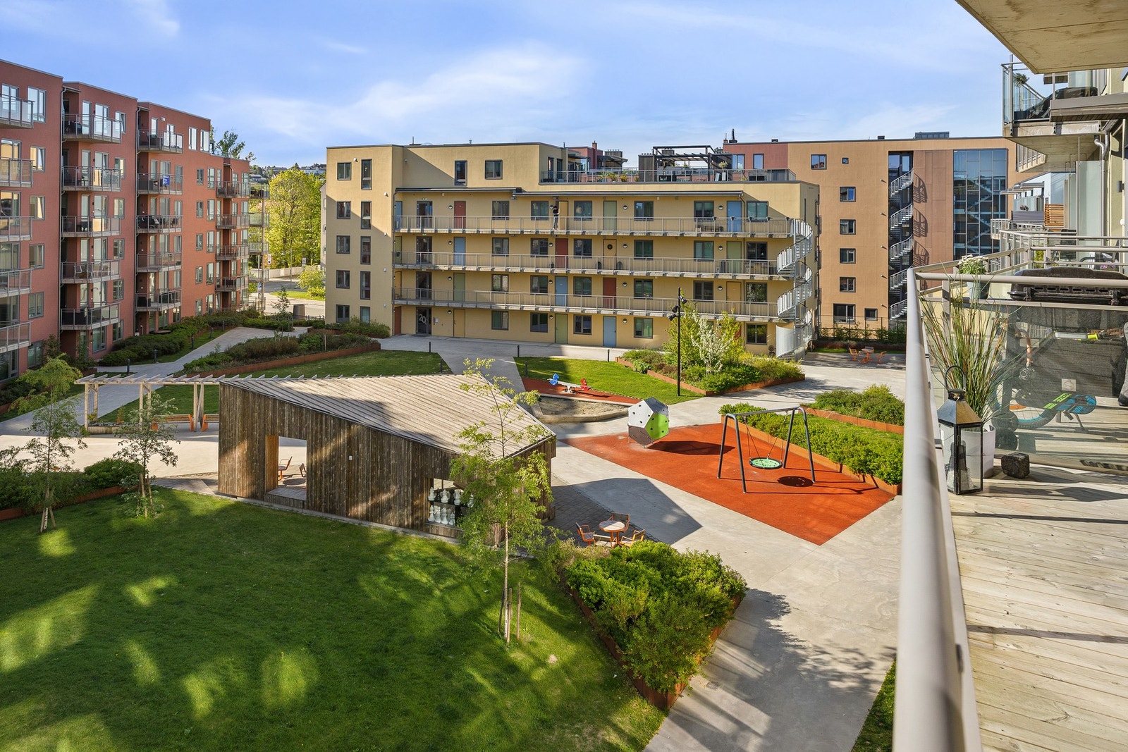 Utsiktsbilde fra balkongen. Pent felles uteområde som er opparbeidet med internstier, ulike lekeapparater og grønne vekster på sommerhalvåret. Galleribilde