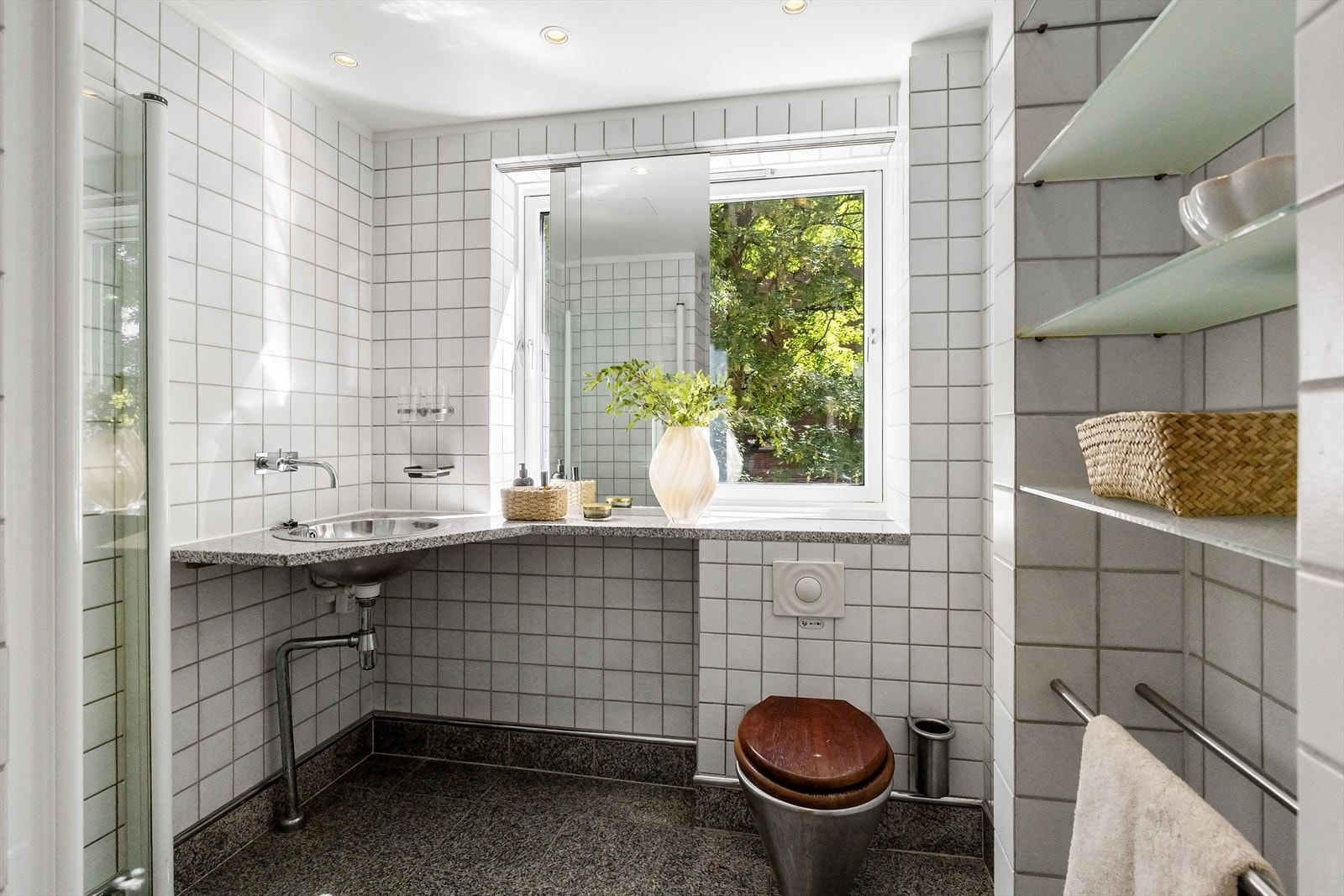 Lyst og luftig bad med dusj, veggmontert toalett, rikelig med benkeplass og innfelte hyller. Galleribilde