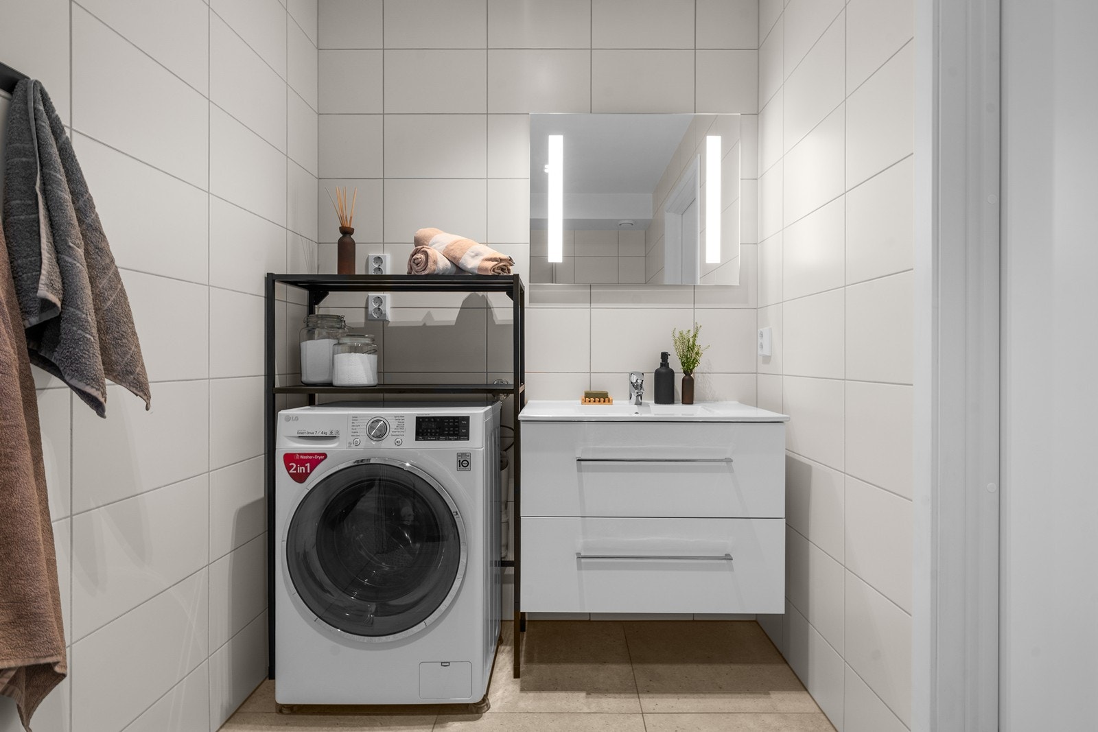 Badet er utstyrt med hvit innredning med servant og skuffer, vegghengt toalett, dusjhjørne med glassdør og opplegg for vaskemaskin. Galleribilde