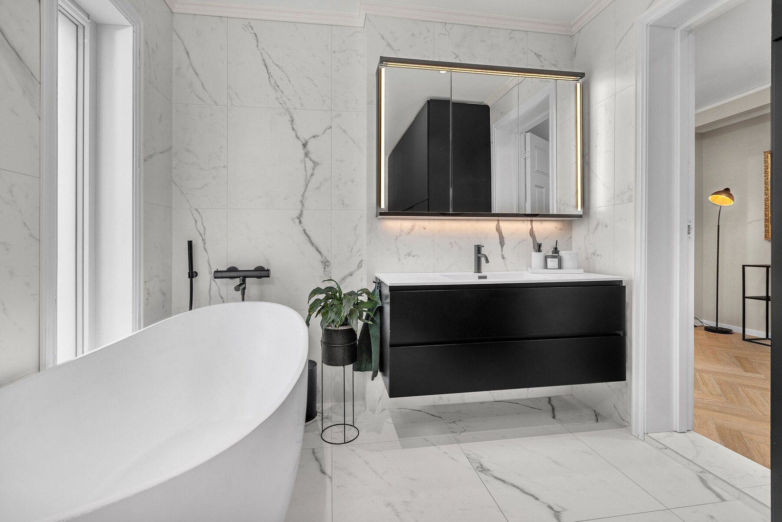Badet er innredet med et frittstående badekar, servantskap med skuffer, høyskap og speilskap med belysning. Galleribilde