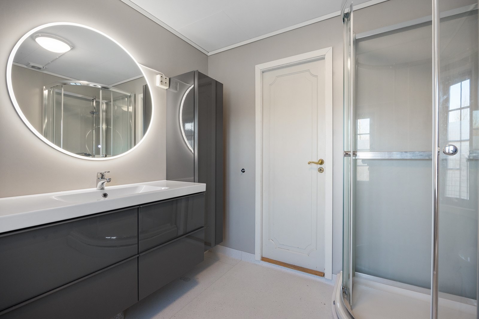 Badet har fliser på gulv med elektrisk gulvvarme, samt platet og malte vegger og malte himlingsplater. Badet er innredet med dusjkabinett, servant med møbler og wc. Galleribilde