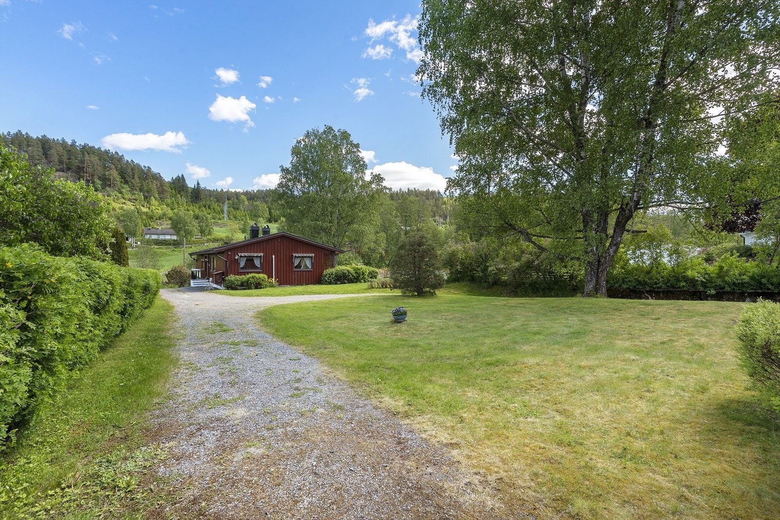 Eiendommen ligger tilbaketrukket fra veien, omkranset av jorder og skog. Galleribilde