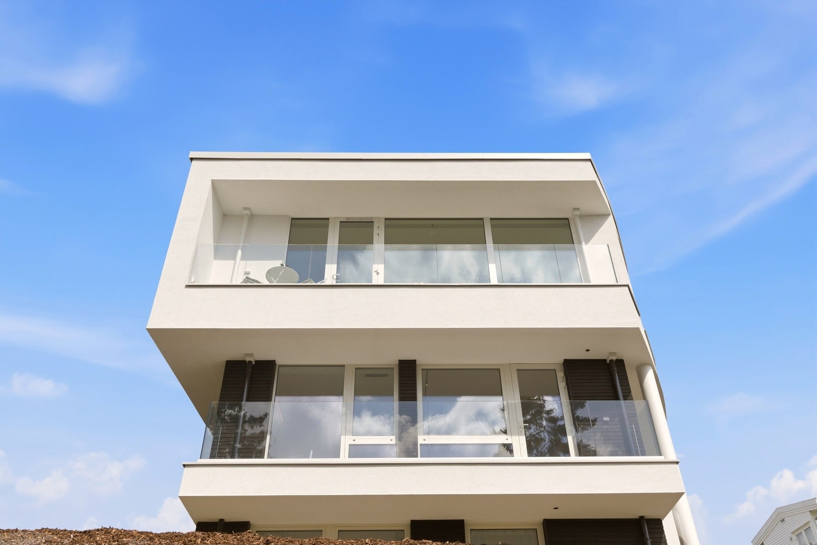 Boligen har et moderne arkitektonisk uttrykk med rene, symmetriske linjer og markerte overheng som gir fasaden både dybde og karakter. De store utkragingene skaper et elegant visuelt uttrykk samtidig som de gir skjerming til balkonger og vindusflater. Galleribilde