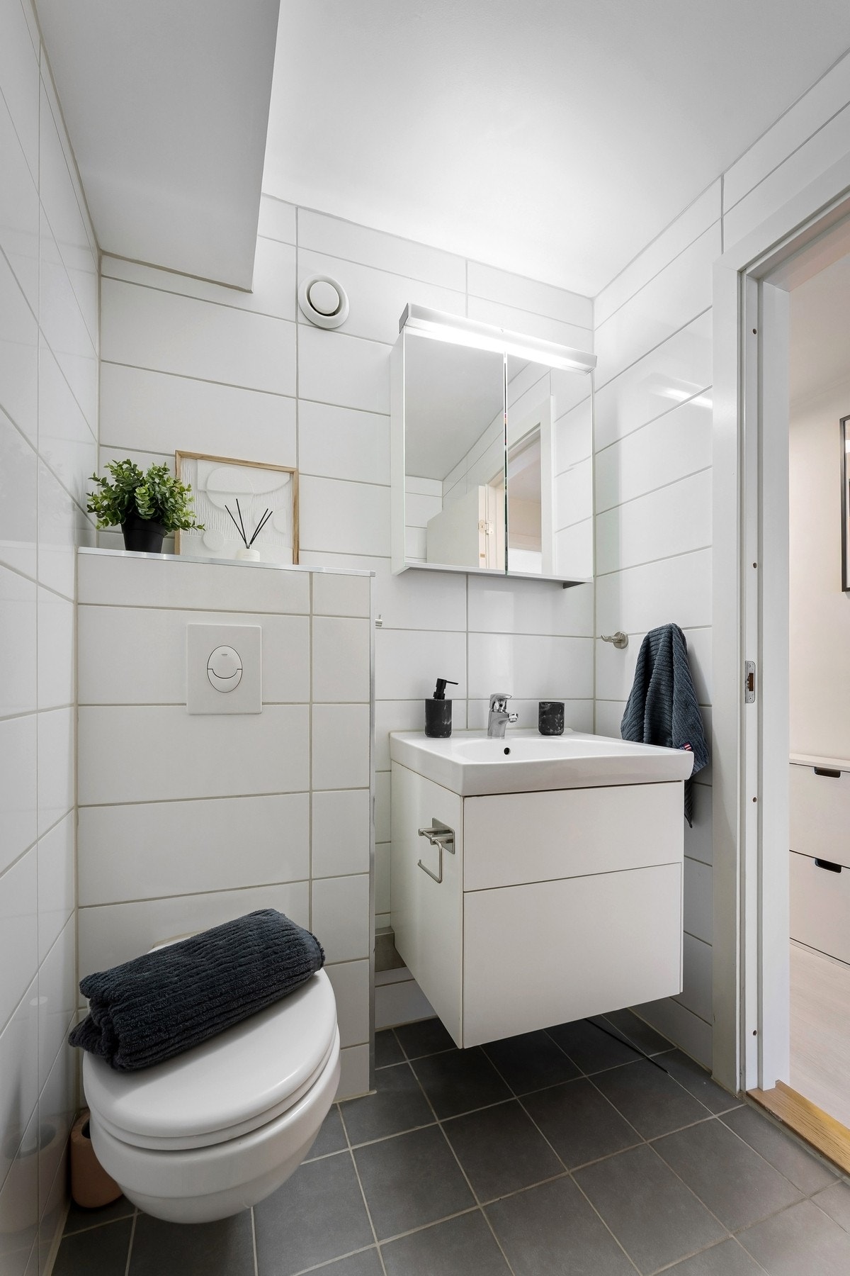 Badet er innredet med vegghengt servantinnredning, vegghengt speilskap med overlys og stikkontakt, dusjhjørne med buet innfellbare glassdører og dusjarmatur tilkoblet veggmontert hånddusj og regndusj, samt vegghengt toalett med innebygget sisterne. Galleribilde