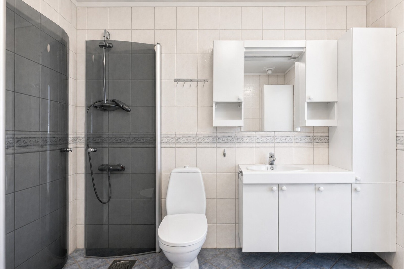 Badet er flislagt og utstyrt med dusjhjørne, toalett og servant med underskap. Galleribilde