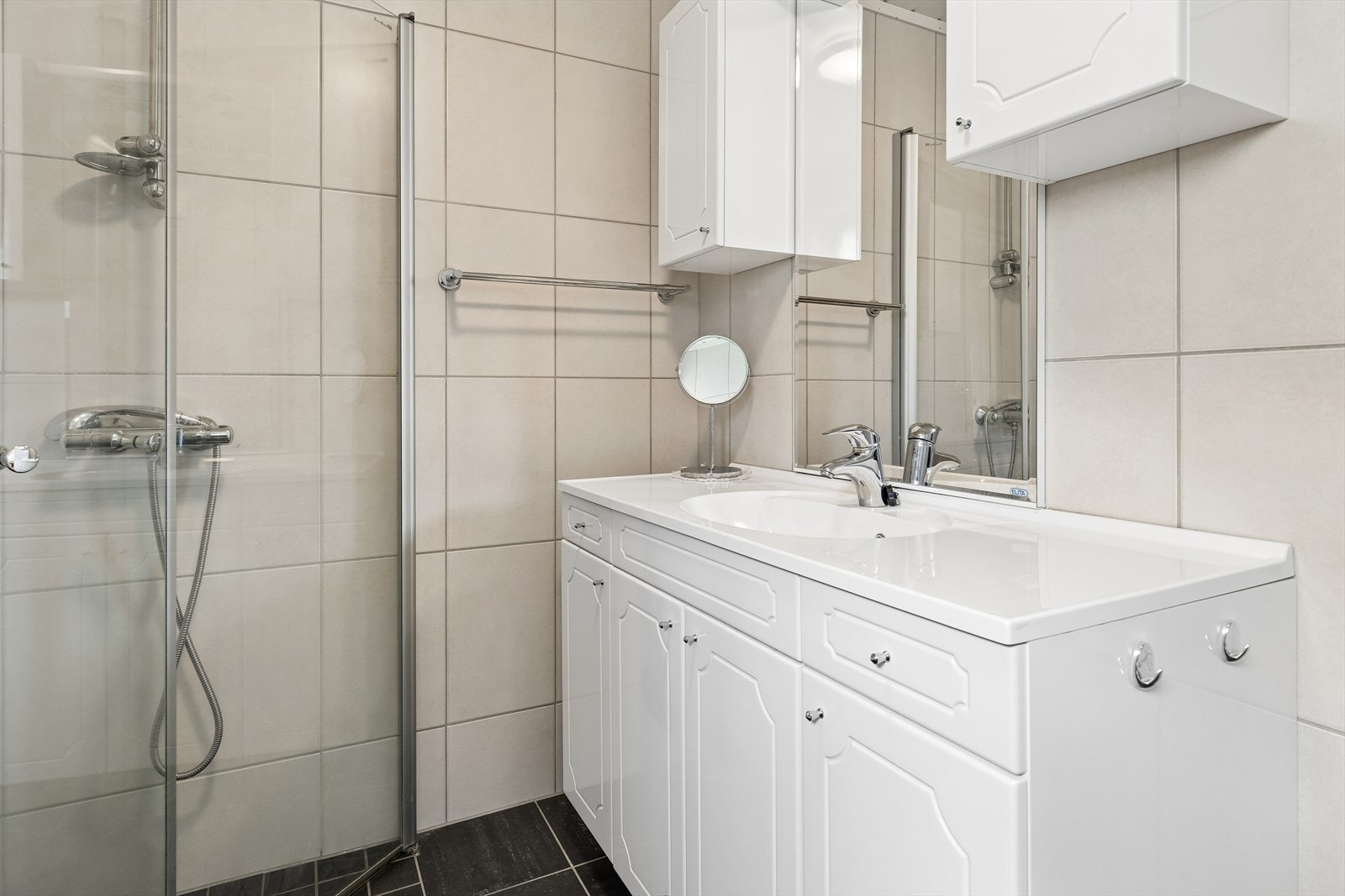 Badet har gulvstående toalett, servant i skapinnredning og dusjhjørne med glassdører. Galleribilde