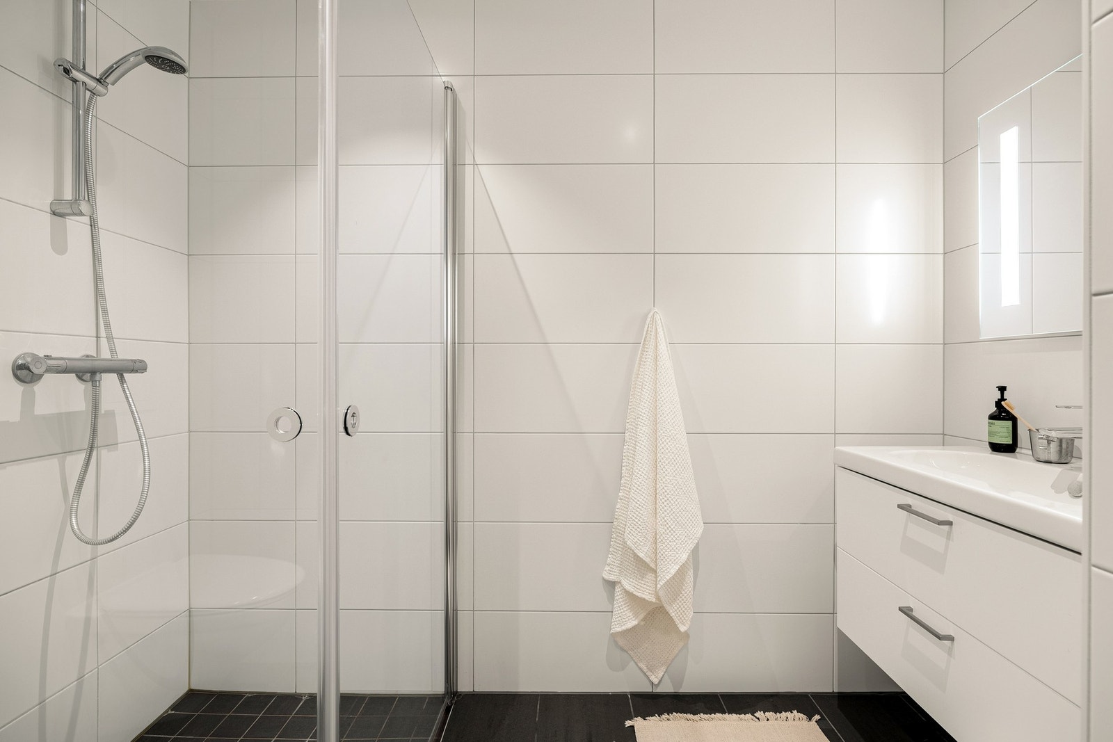 Badet er innredet med vegghengt toalett, dusjhjørne med glassvegger, og baderomsmøblement med speil og belysning. Galleribilde