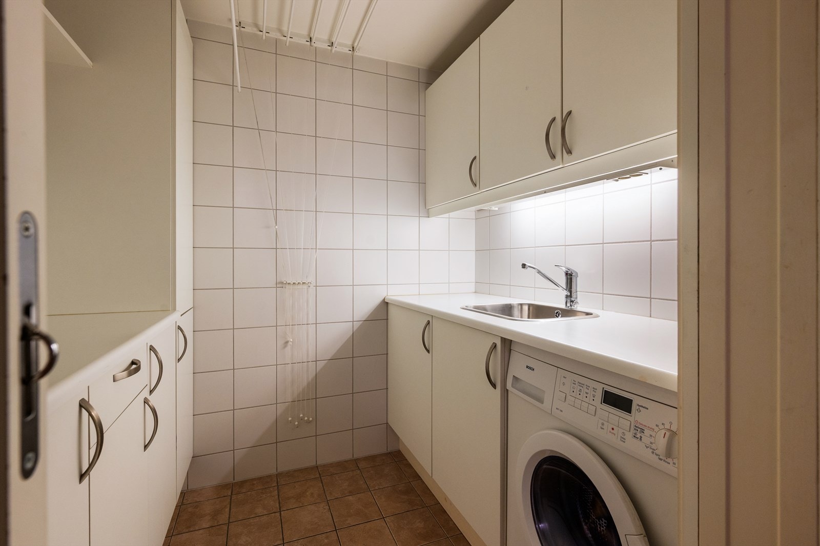 Egen vaskeromssone med opplegg for vaskemaskin, arbeidsbenk og oppbevaringsskap. Galleribilde