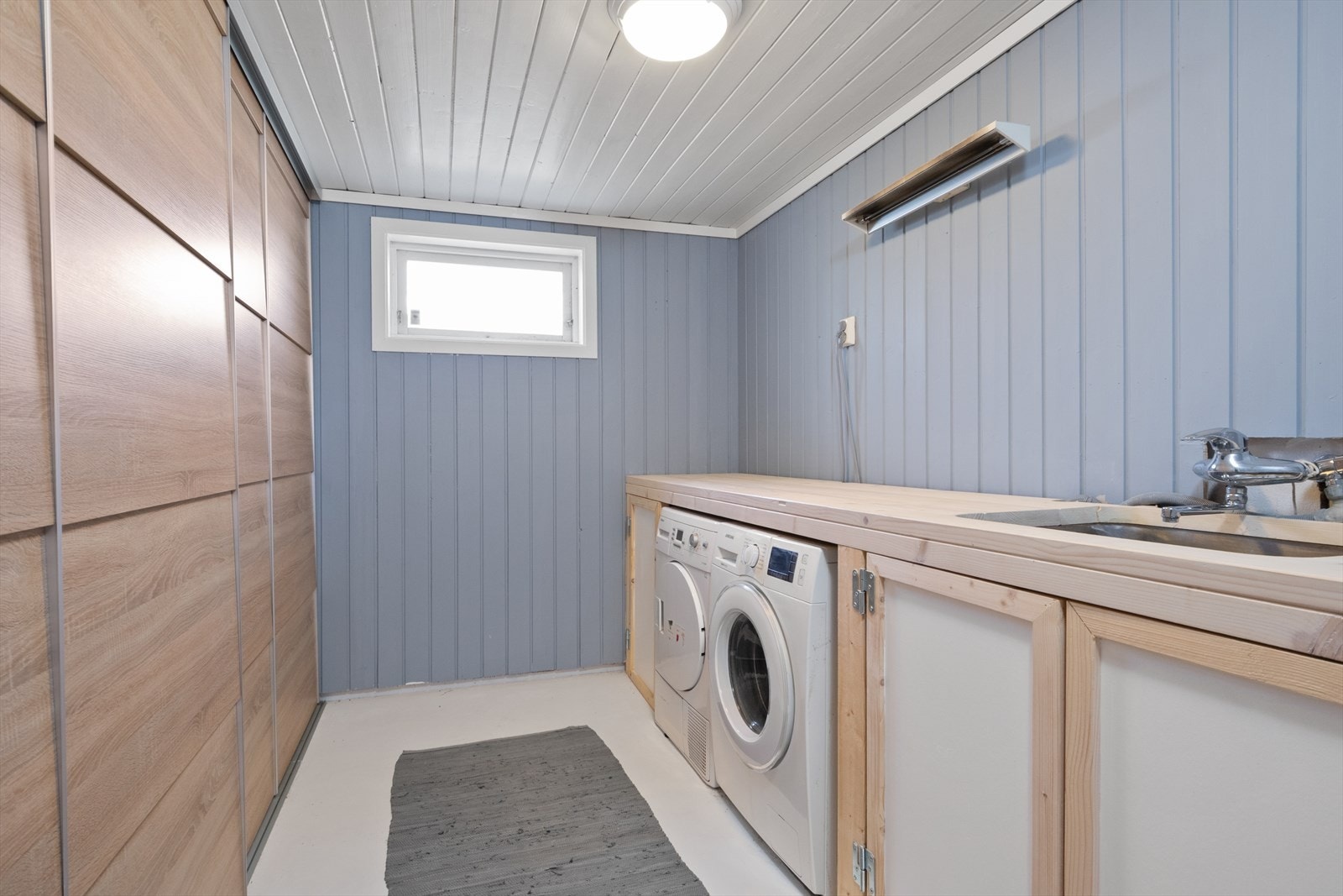 Praktisk vaskerom med plassbygget innredning, opplegg for vaskemaskin og god lagringsplass i skyvedørsgarderobe. Galleribilde