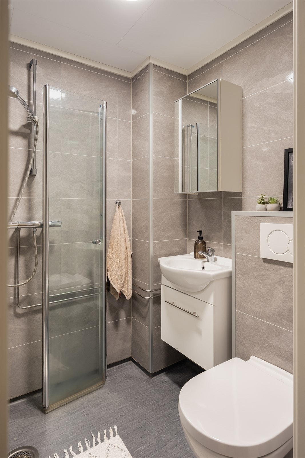 Badet er utstyrt med vegghengt toalett, baderomsinnredning og innfellbare dusjvegger av glass. Galleribilde