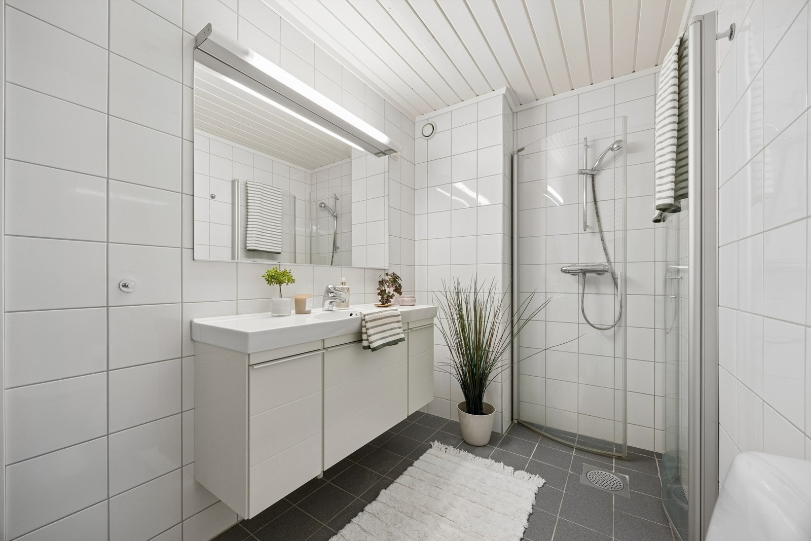 Badet er helflislagt i hvitt med mørke gulvfliser og har dusjhjørne med glassdør, vegghengt servant og god belysning. Alt er delikat og funksjonelt - akkurat det man trenger. Galleribilde