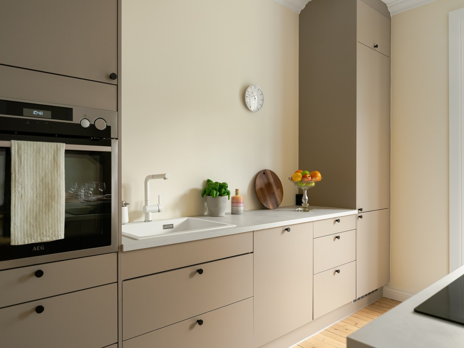 Kjøkkenet har beige, slette fronter og en tynn, hvit benkeplate i laminat for et stramt uttrykk. Galleribilde
