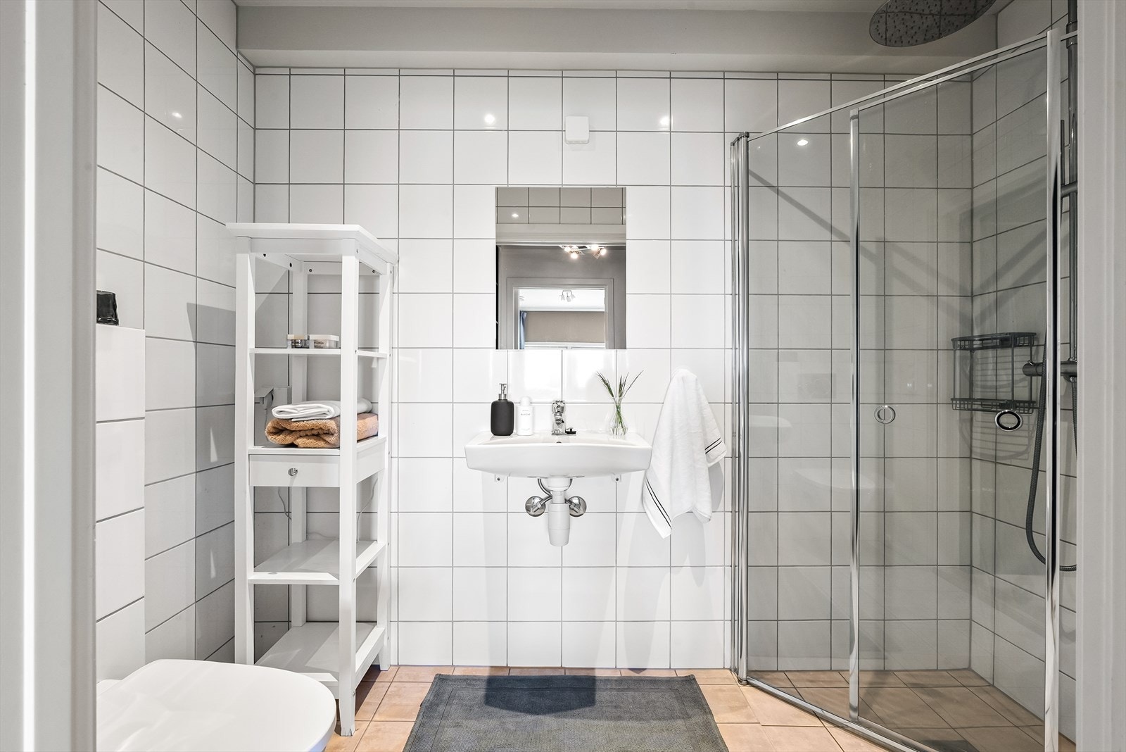 Helfliset bad i underetasje med varmekabler i gulv og downlights i himling. Innredet med vegghengt toalett, servant og dusjhjørne med regnfallsdusj Galleribilde