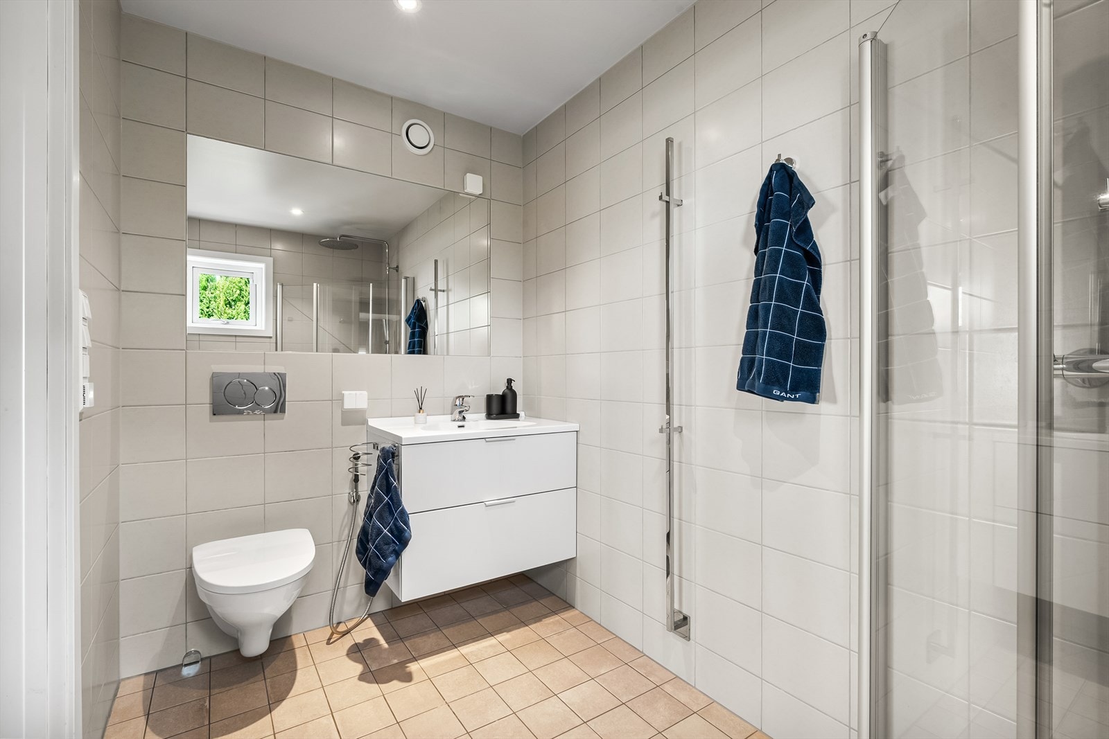 Helfliset bad i 1. etasje med vindu, varmekabler i gulv og downlights i himling. Innredet med vegghengt toalett og baderomsinnredning. Dusjhjørne med innfellbare glassdører og regnfallsdusj Galleribilde