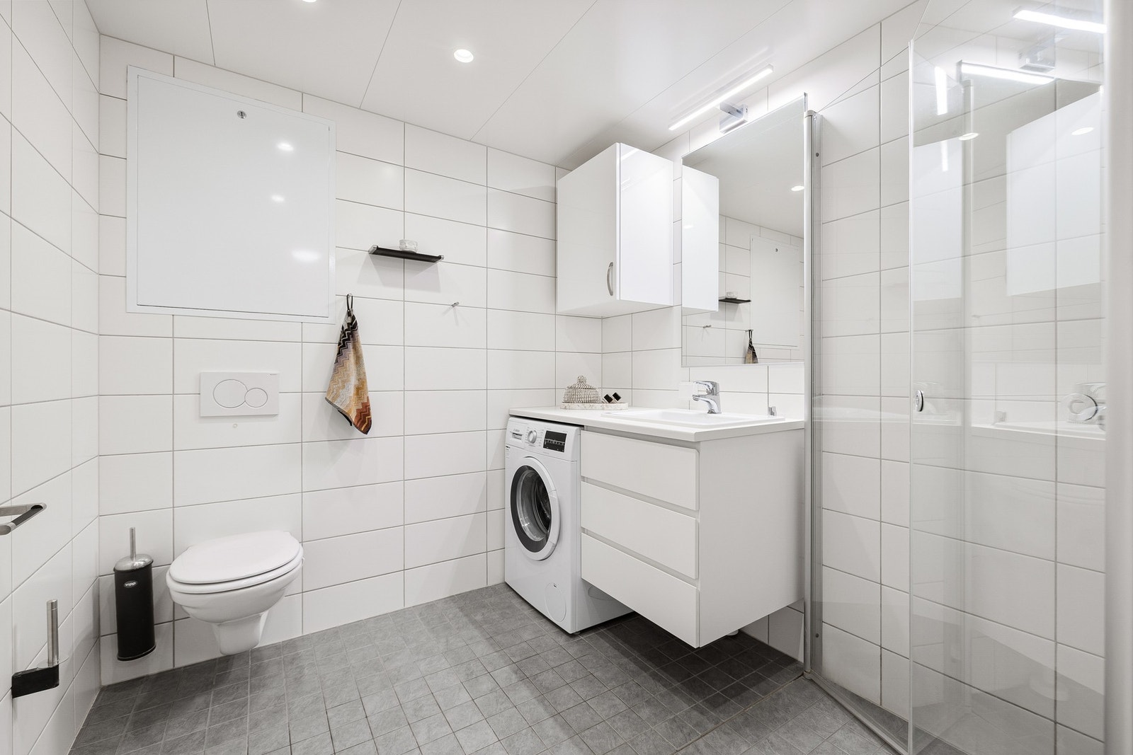 Pent flislagt bad på 4,6 kvm. Badet er utstyrt med varmekabler i gulv, veggehengt toalett og innfellbare dusjdører i glass. Galleribilde